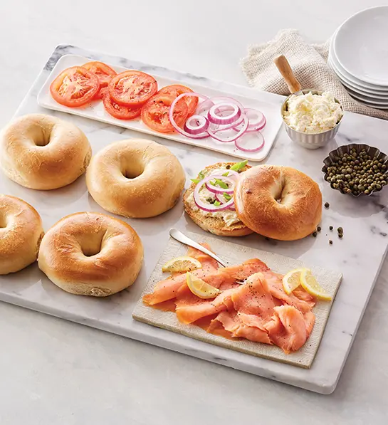 A photo of gift baskets with a display of bagels and lox on a marble cutting board with cream cheese