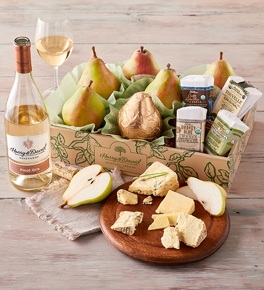 A photo of gift baskets with a box of pears and cheese next to an open bottle of wine and full glass with a plate of sliced pears and cheese in front