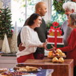 A photo of gift baskets with two couples exchanging a gift tower in a house decorated for Christmas