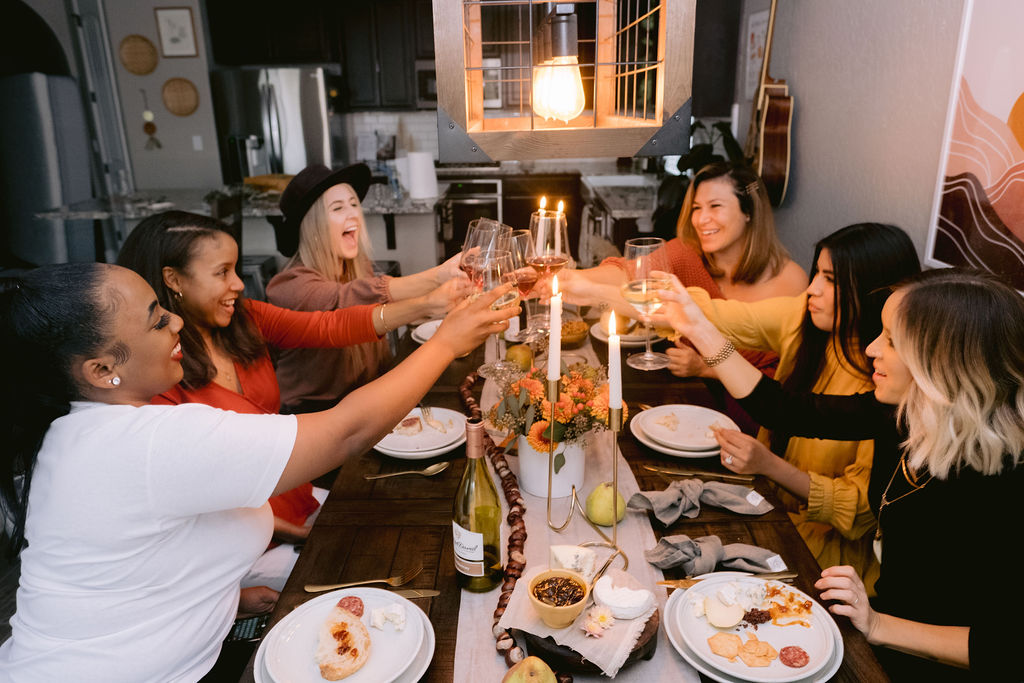 A photo of how to celebrate Kwanzaa with a group of women clinking glasses of wine at a table.