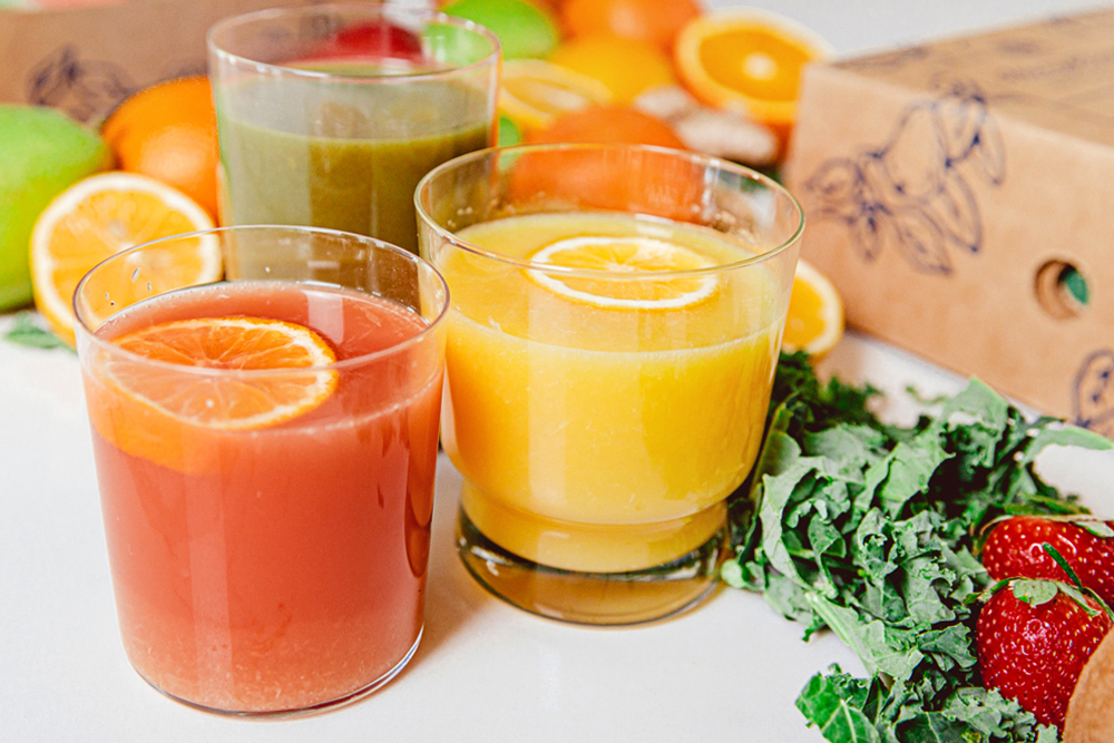 A photo of fruit juice recipes with three glasses of fruit juice surrounded by raw ingredients