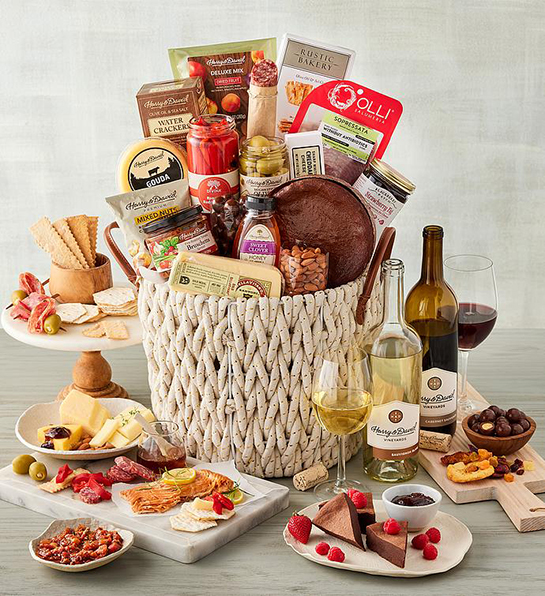 Best gift basket full of cheese, meat, crackers, sweets and more surrounded by the same items and two bottles of wine.