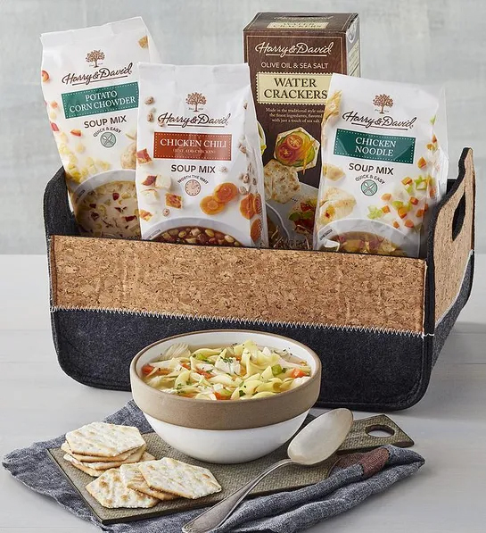 Best gift basket full of three bags of soup mixes and a box of crackers sitting next to a bowl of soup.