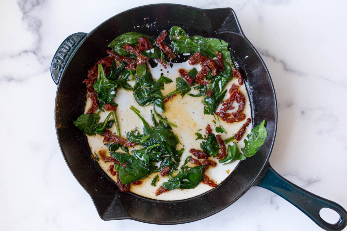 Cast iron salmon recipe with a cast iron skillet full of spinach, sauce and sun dried tomatoes.