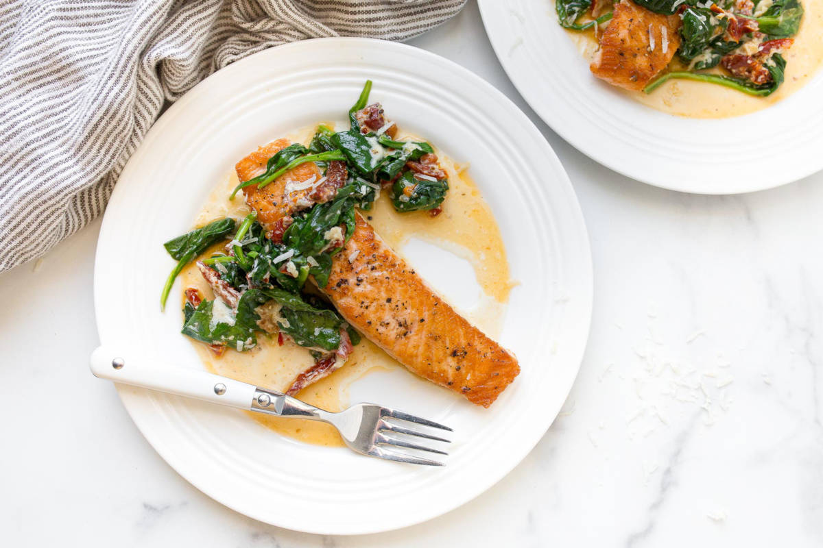 Cast iron salmon on a plate with spinach and sun dried tomato on top.