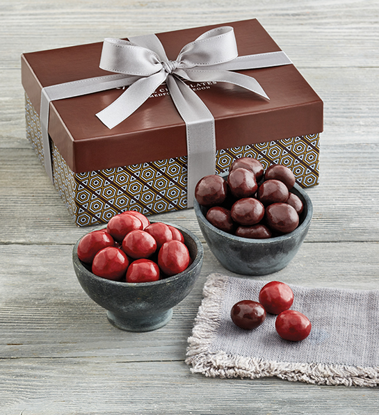 Una foto de rellenos de canastas de Pascua que muestran dos tazones de cerezas cubiertas de chocolate y una caja detrás de los tazones