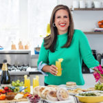 A photo of Easter meal with a woman holding a mimosa standing in front of an Easter brunch spread