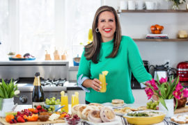 A photo of Easter meal with a woman holding a mimosa standing in front of an Easter brunch spread