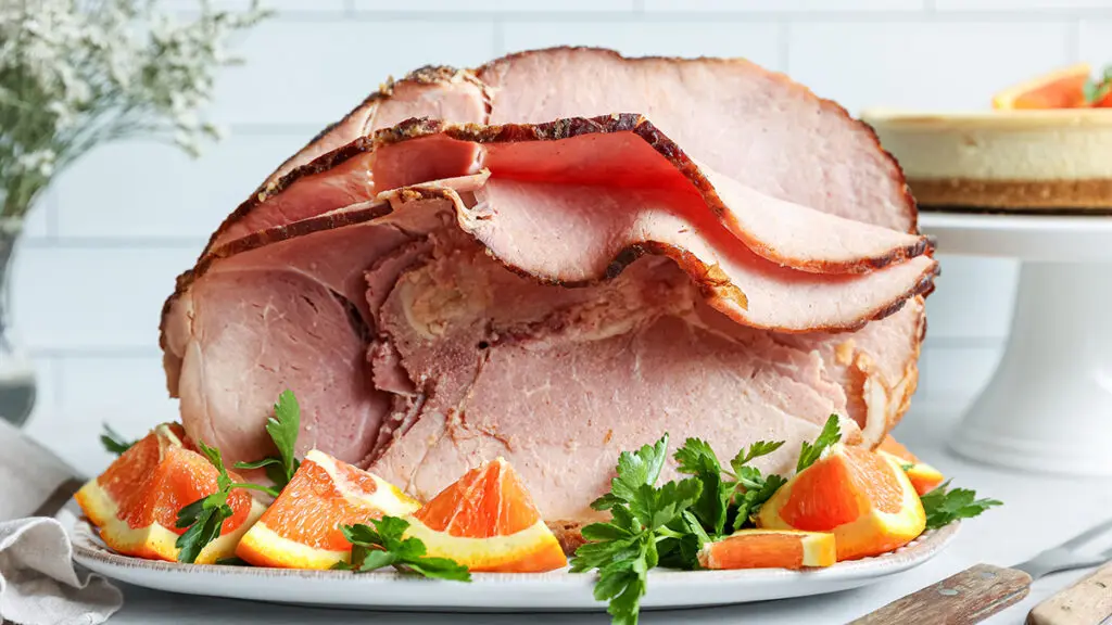 How to cook ham with a large ham on a plate with orange garnish.