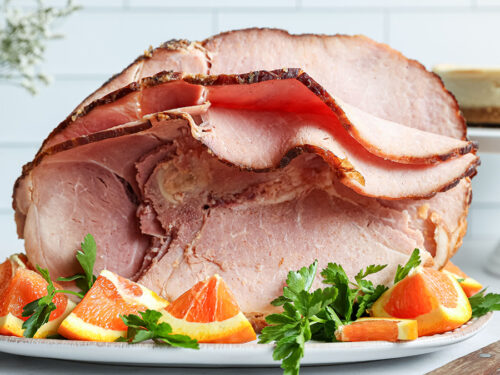 How to cook ham with a large ham on a plate with orange garnish.