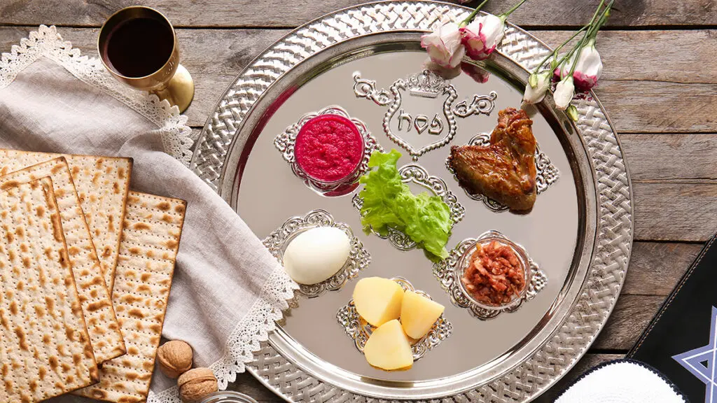 Passover food traditions with a seder plate set with items of food next to matzah and a glass of wine.