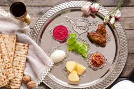 Passover food traditions with a seder plate set with items of food next to matzah and a glass of wine.