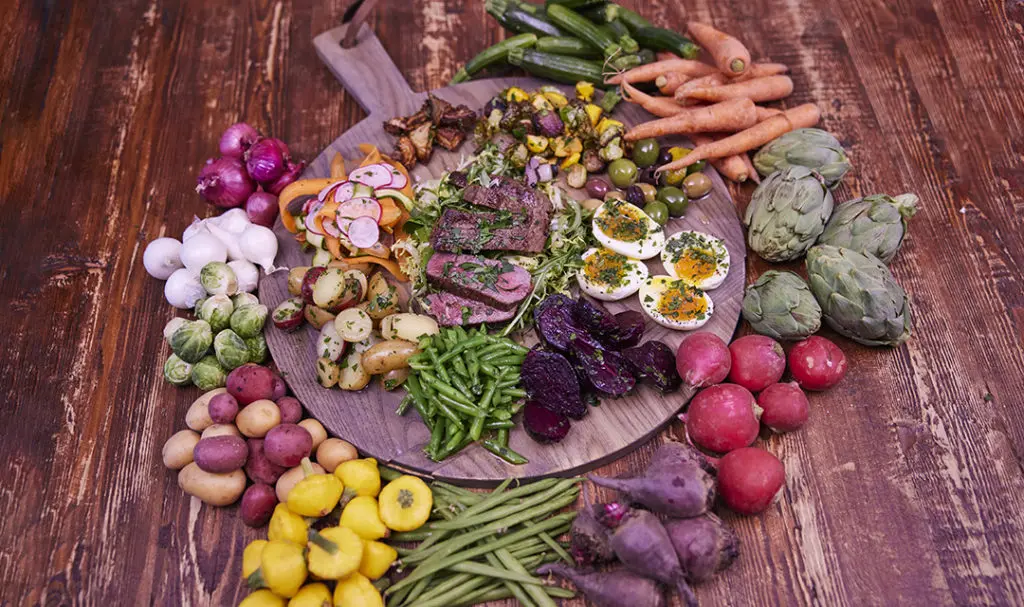 A photo of Father's Day recipes with a board full of steak and roasted and seared vegetables surrounded by raw vegetables.