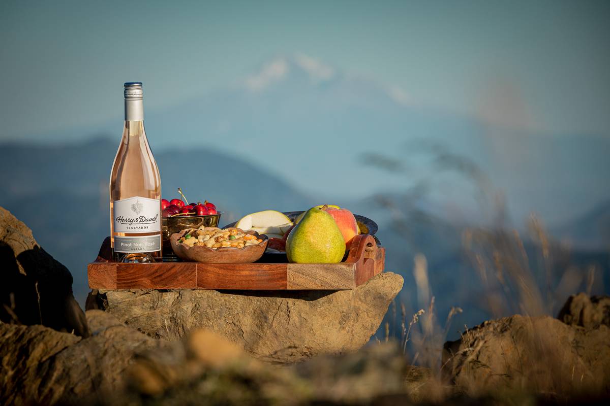 Wines for spring with a bottle of rosé on a wooden platter with fruit and nuts balanced on a rock.