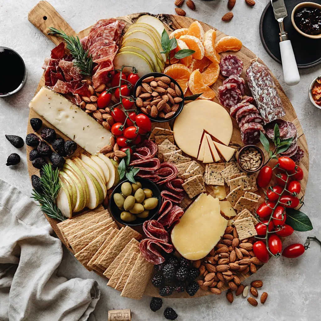 Photo of charcuterie board with an arrange of meats, cheese, nuts, fruit and garnishes.