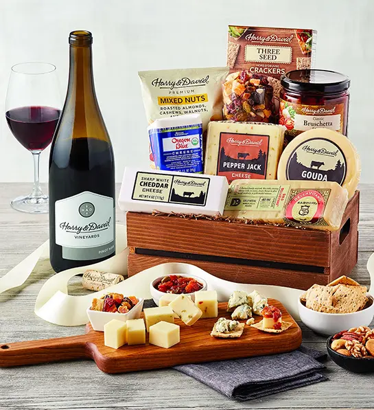 Last minute gift ideas for mom with a box full of cheese, crackers, and other savory snacks with the same items surrounding the box and a bottle of wine.