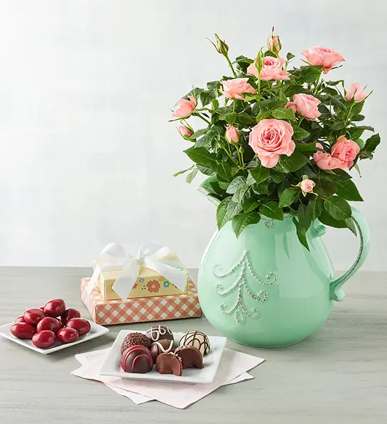 Mother's Day gift ideas with a pitcher of flowers next to a collection of sweet treats and truffles.