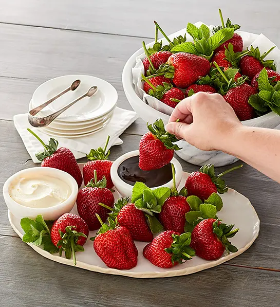 Mother's Day gift ideas with two plates of strawberries and a hand dipping a strawberry in a bowl of chocolate sauce.