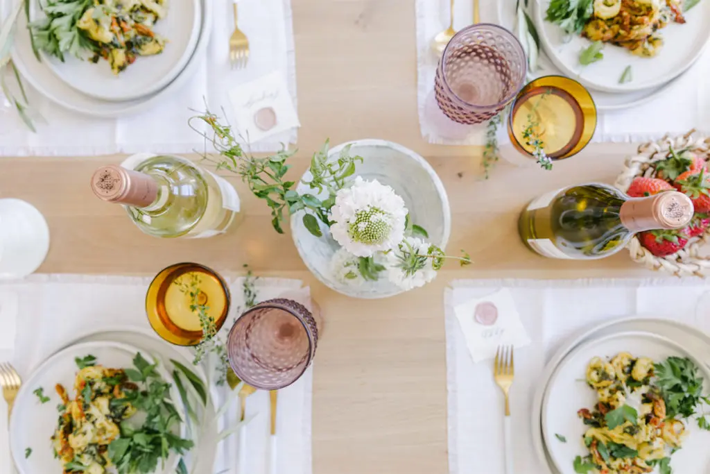 Birthday party dinner with flowers, bottles of wine, and plates of food on a table.