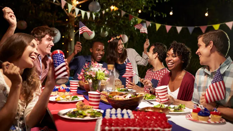 Photo of fourth of july celebration with a group friends sitting at a table laughing.