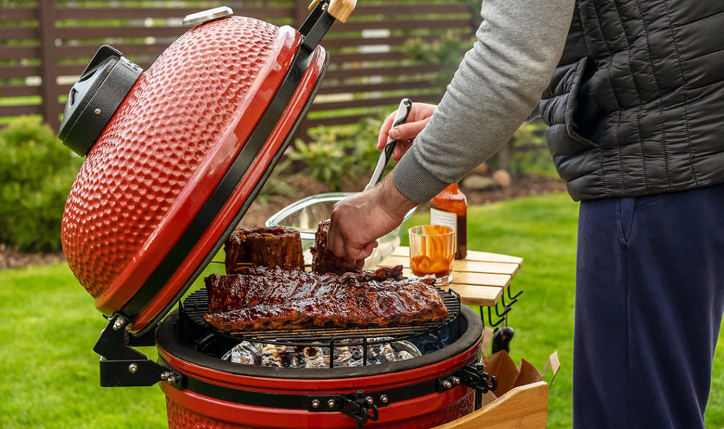 Grill guide with a kamado grill half open with someone grilling several racks of meat on it.