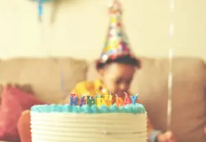 Birthday traditions image - baby sitting in the background while a birthday cake rests in the foreground