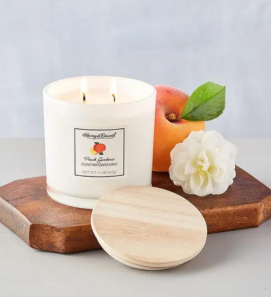 A photo of birthday gift ideas with a burning candle on a wooden board with a peach and a flower next to it.