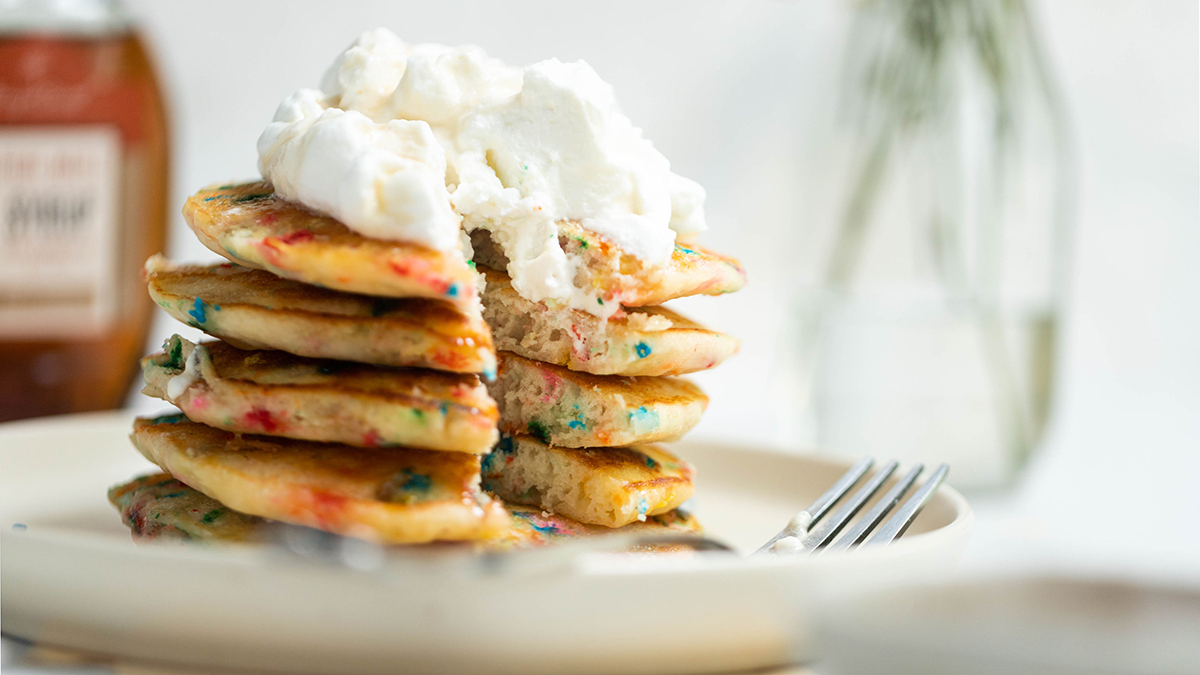 A photo of confetti pancakes stacked on a plate topped with whipped cream