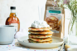 A photo of confetti pancakes on a plate topped with whipped cream and candles