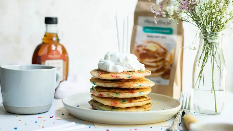 A photo of confetti pancakes on a plate topped with whipped cream and candles