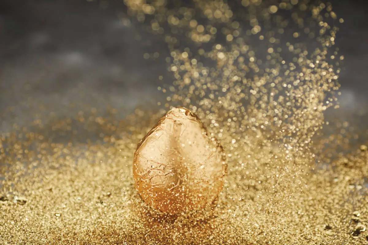 A photo of a gold pear with gold sparkles all around it