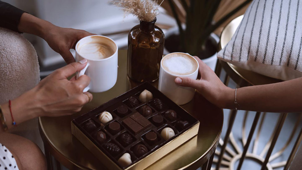 A photo of teacher gifts with a box of chocolates on a table with two cups of coffee