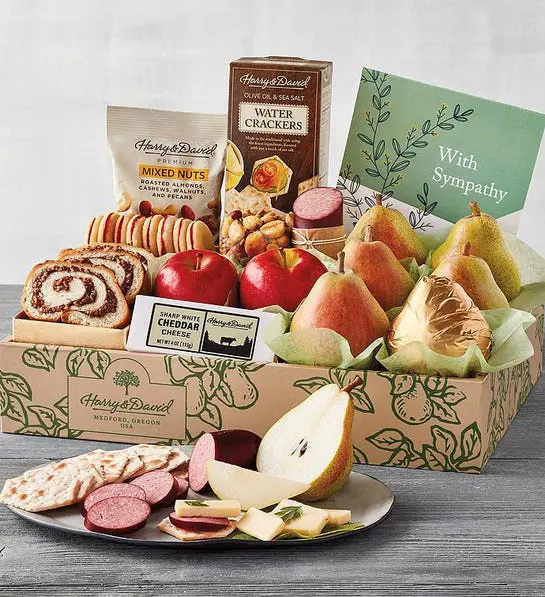 Sympathy gift ideas image - Harry & David Deluxe Sympathy Gift Box with sliced pear, sausage, cheese and crackers on a plate in front of the box.