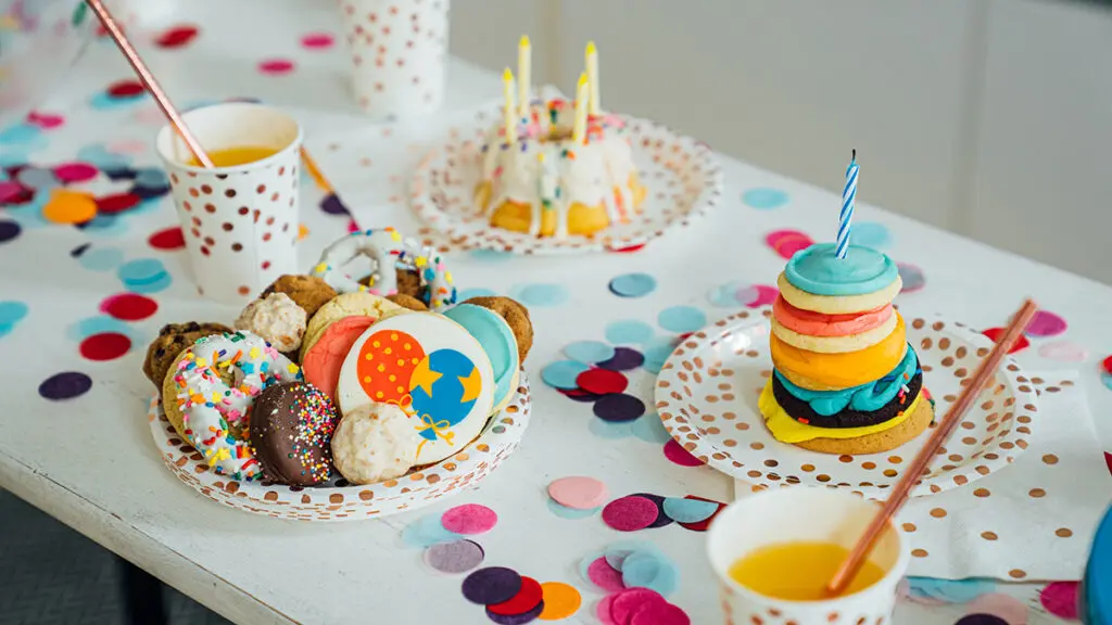 Birthday tradition image - birthday cake and cookies with candles on confetti covered table.