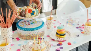 Birthday traditions around the world image - birthday cake and candles on a table with someone setting down a plate of cookies.