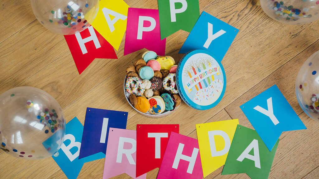 Birthday traditions around the world image - happy birthday banner on a table surrounding a tin of cookies