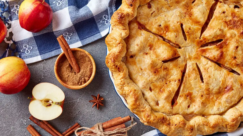 Apple image - overhead view of Freshly baked delicious classic homemade American apple pie on a concrete table with kitchen towel and ingredients, view from above, close-up, macro