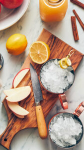 Moscow mule recipe image - cups filled with ice on a cutting board with chopped apples and lemons