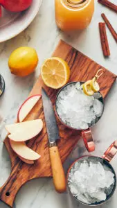Moscow mule recipe image - cups filled with ice on a cutting board with chopped apples and lemons
