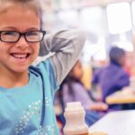 hunger and food insecurity image - young girl with glasses smiling at a school lunch table.