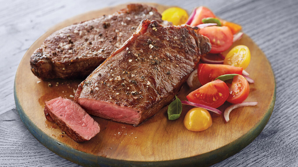 New York Strip Steak image - New York strip steak on board with fresh tomatoes