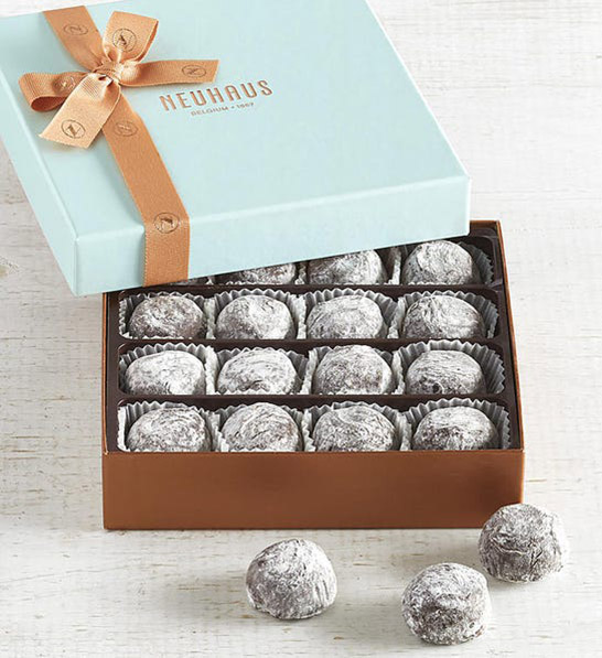 anniversary gift guide image - champagne truffles in a gold and blue box with three truffles sitting outside of it.