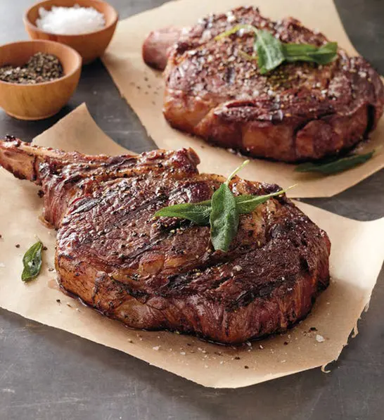 anniversary gift guide image - grilled bone-in ribeye steak on wax paper with spices in the background.