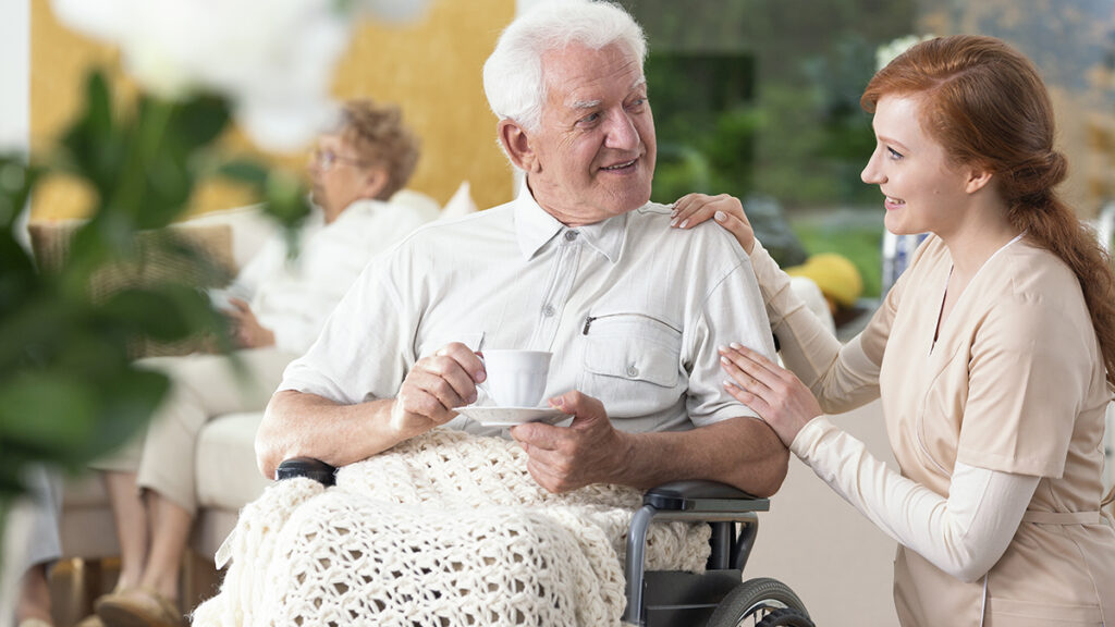 gifts for caregivers image - older man in a wheel chair with young nurse talking to him.