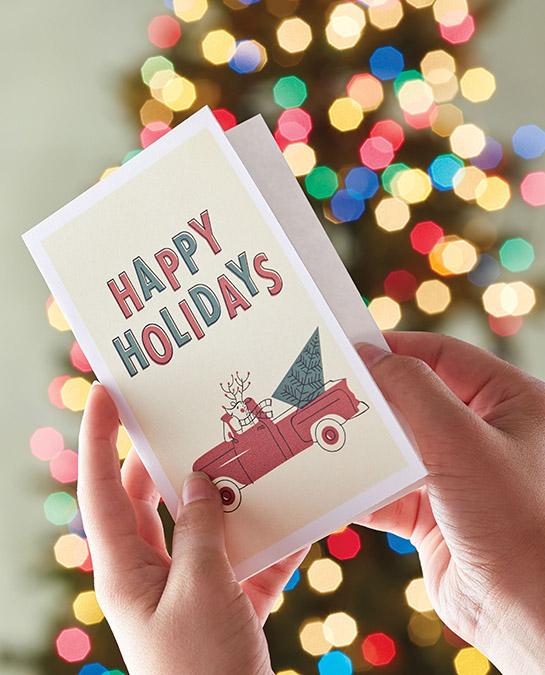 christmas quotes image - hands opening a christmas card with christmas tree in the background