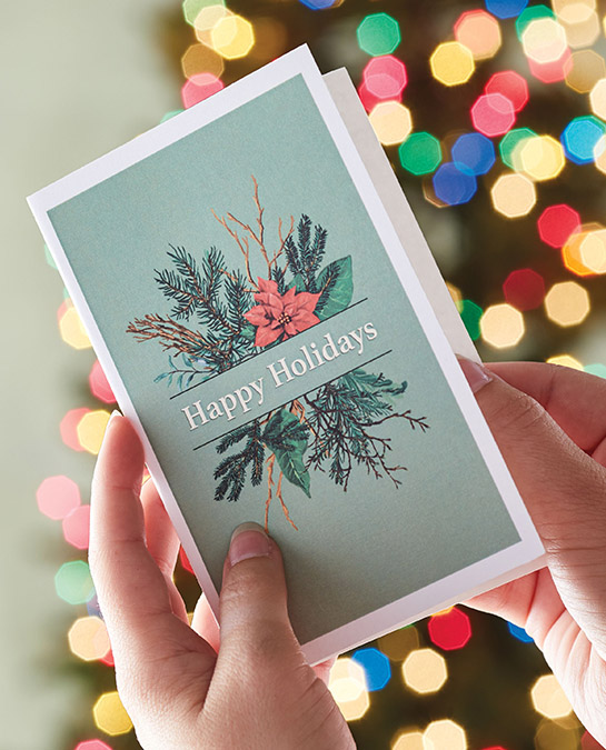 christmas quotes image - hands opening a christmas card with christmas tree in the background