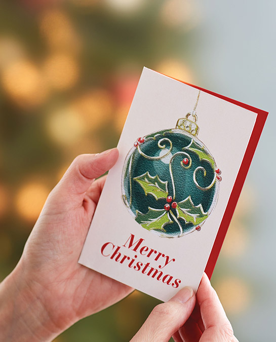 christmas quotes image - hands opening a christmas card with christmas tree in the background