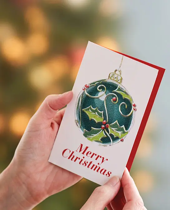 christmas quotes image - hands opening a christmas card with christmas tree in the background