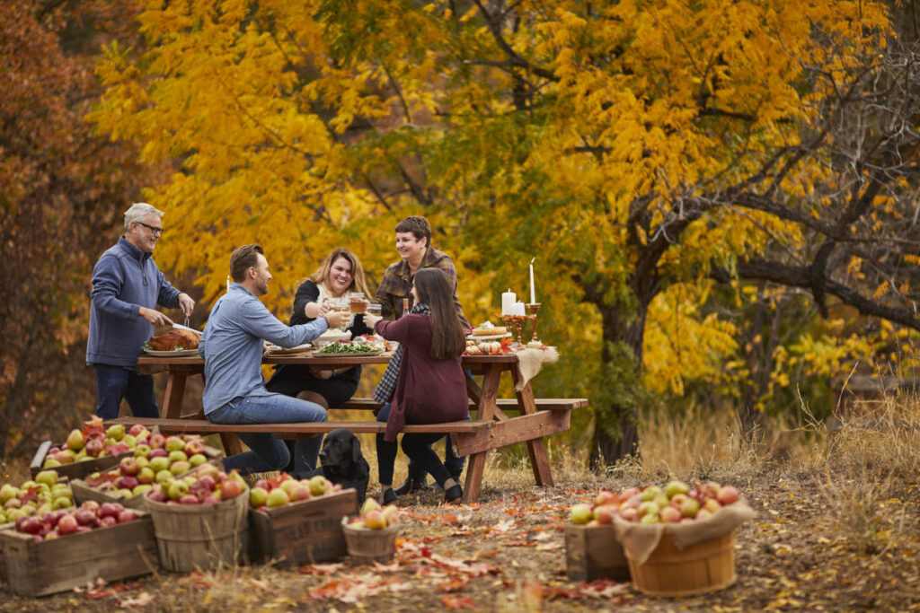 fall leaves image - group of people having dinner outside surrounded by fall leaves and barrels of apples