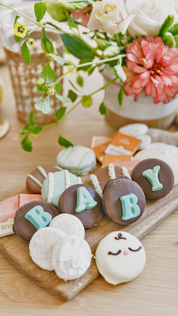 host a baby shower image - cookies displayed on a board with flowers in the background.